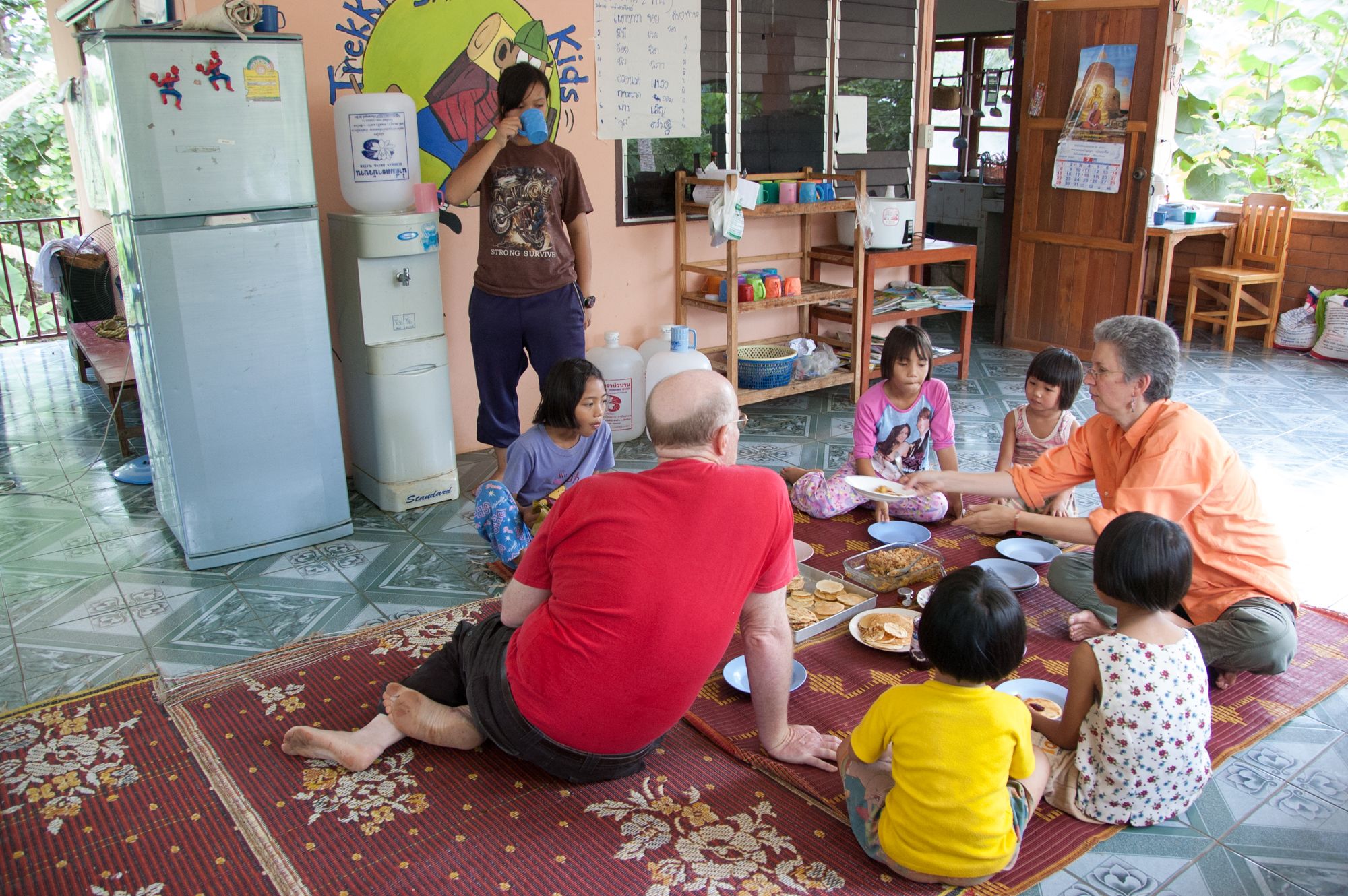 A group of eight dine together on a mat rolled out on the kitchen floor